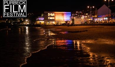The Mowlem Theatre in Swanage at night with the waves lapping at the beach and the foot of the cinema