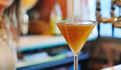 Someone pouring a pornstar martini into a glass