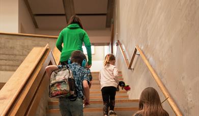 Children with sensory backpack and ear defenders walking up stairs inside Dorset Museum & Art Gallery.