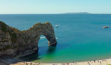 The rock arch at Durdle Door with the beach in front and Portland in the distance.