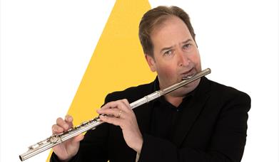 A man is playing the flute in front of a large yellow triangle graphic