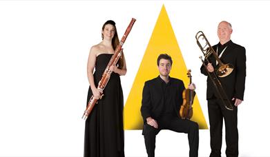 Three musicians are stood in front of a graphic of a yellow triangle.