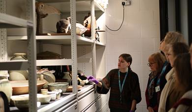 Member of the Collections Team pointing to objects in a display case for group of people.