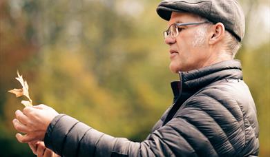 Man in flat cap and puffer coat looking at a leaf