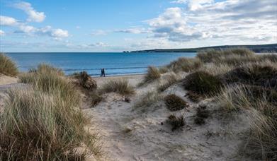 Rugged sand dunes in the foreground with sandy path to beach and Old Harry Rocks in the distance