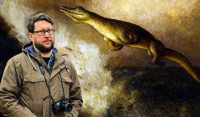 A man with a camera stood in front of an enlarged illustration of a marine reptile.