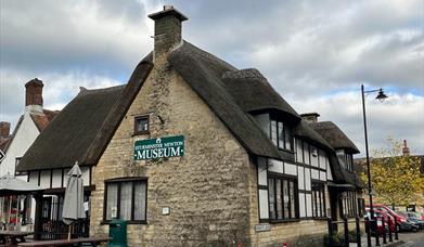 The Sturminster Newton Museum, as seen from the road The museum is a historic cottage with a thatched roof and a green sign.