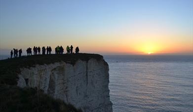 An image of Old Harry Rocks at sunrise with a group standing and watching it