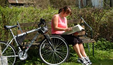 Woman sitting on a bench next to a bike, reading a map.