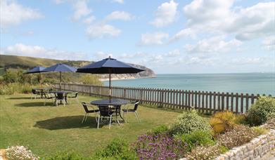 The garden at The Pines Hotel with table, chairs and parasols, overlooking Swanage Bay in Dorset