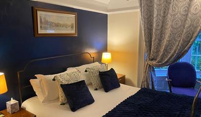 A recently refreshed king bedroom with a comfortable king-size bed dressed in white bedding and a navy throw, set against a deep blue feature wall. Ma