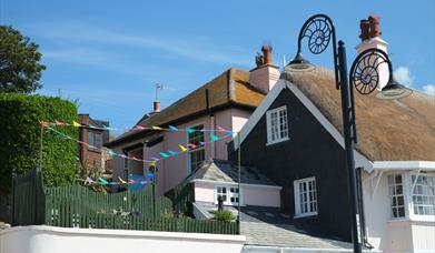 Quaint pink cottage behind iconic thatched cottages on seafront with garden overlooking Lyme Bay.